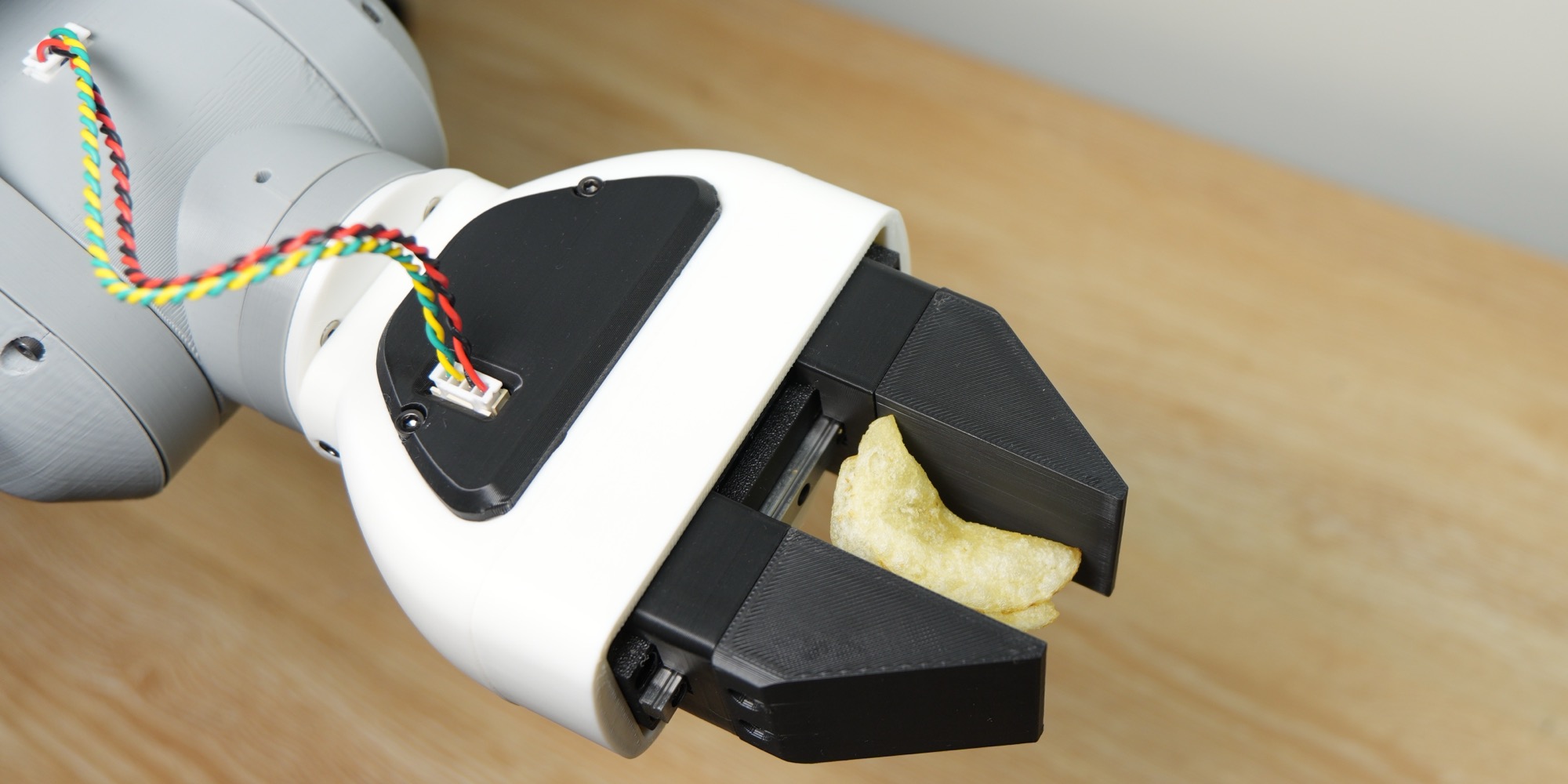 The gripper on the end of a robot arm, holding a potato chip between its black fingers
