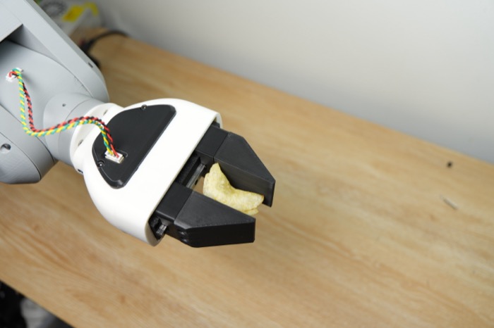 The gripper on the end of the robot arm, holding a potato chip above a wooden table