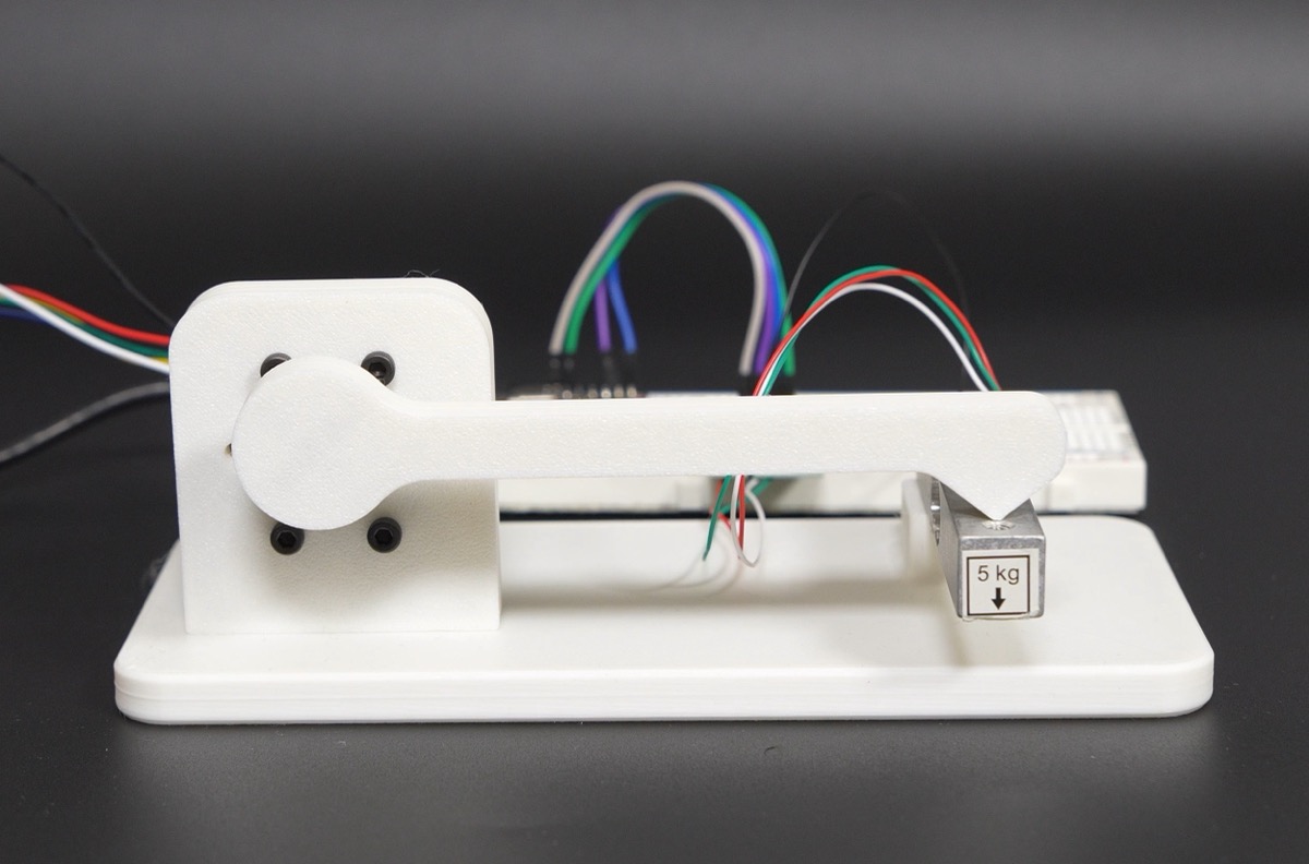 Torque test rig: a white 3D-printed lever arm on the motor shaft rests on a 5 kg load cell