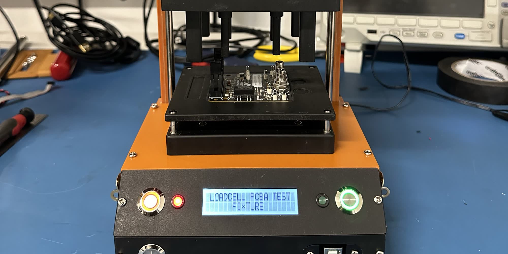 Test fixture with a board clamped on the pogo pin tray; the LCD reads LOADCELL PCBA TEST FIXTURE