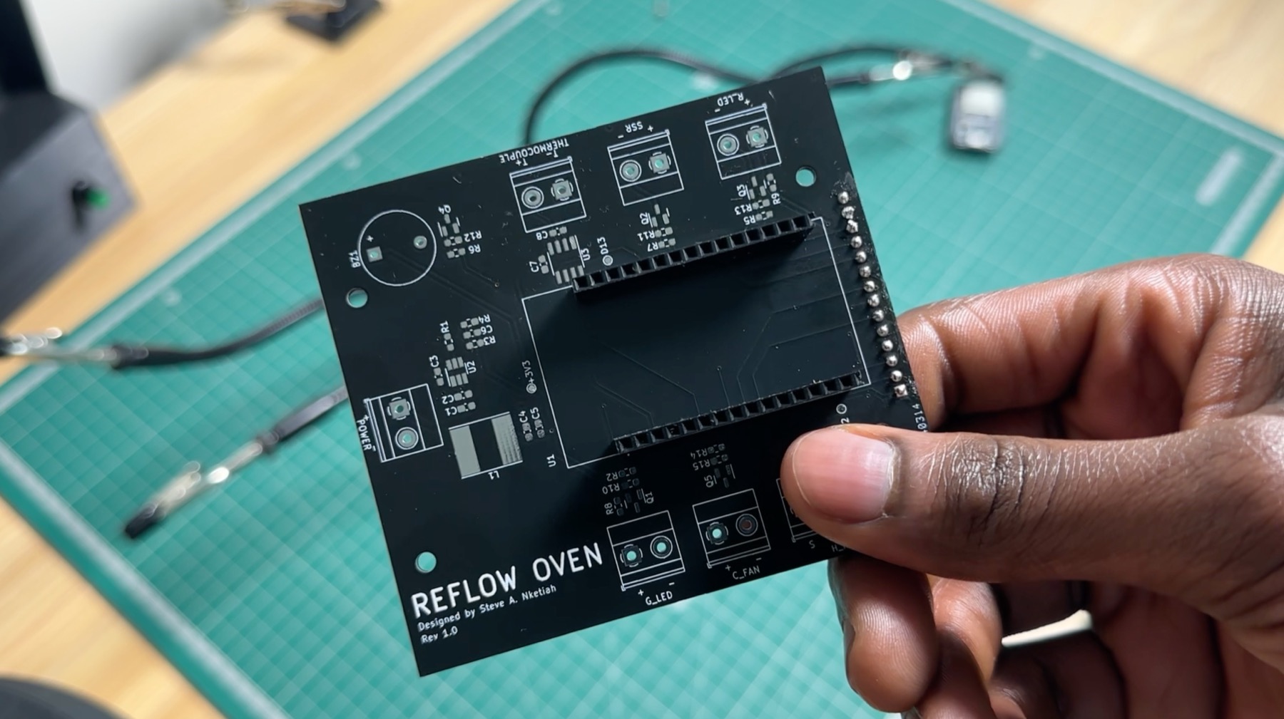 The bare black reflow oven PCB held in a hand
