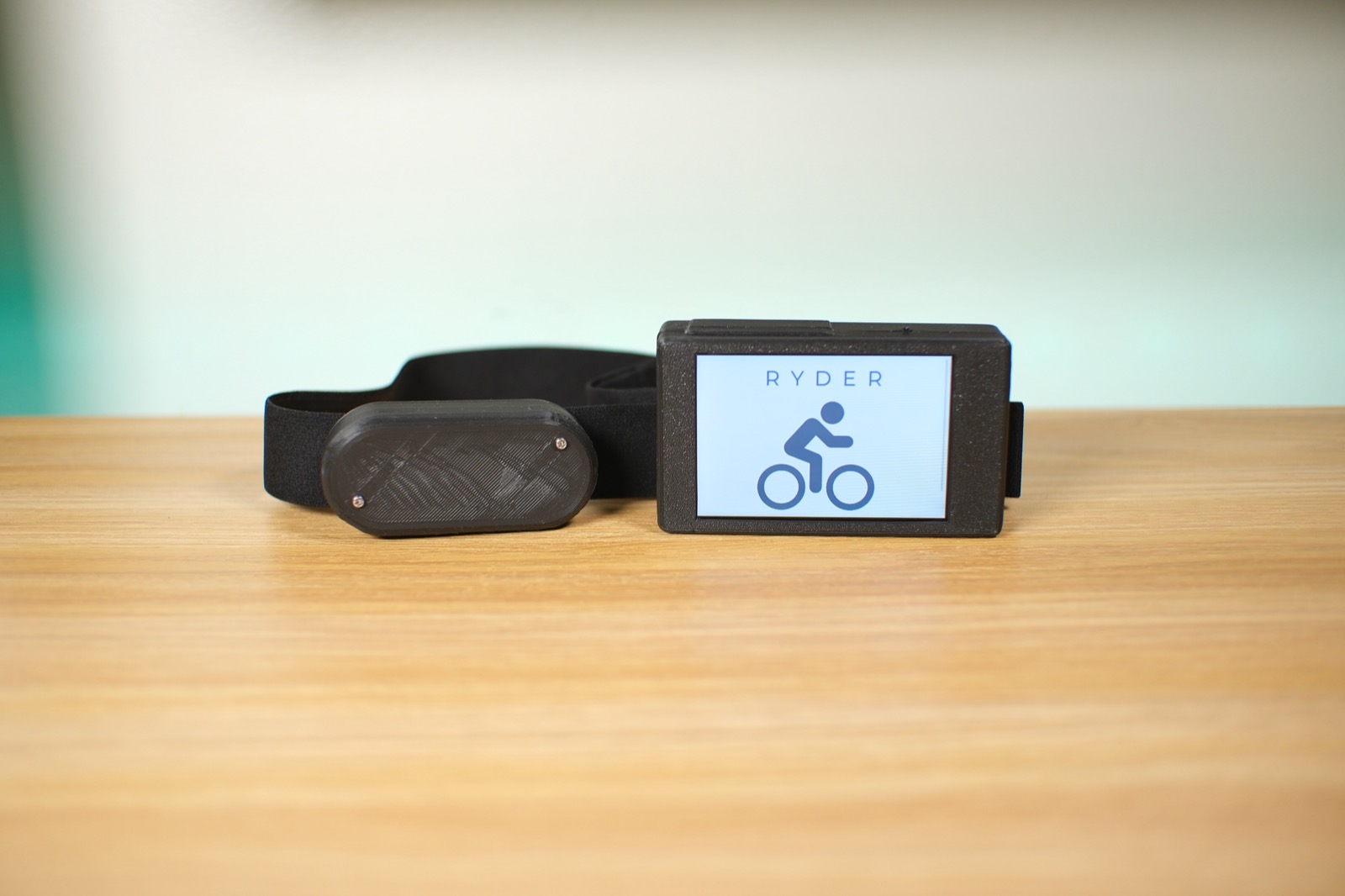 The Ryder ECG chest strap next to the handlebar unit, whose screen shows the Ryder logo